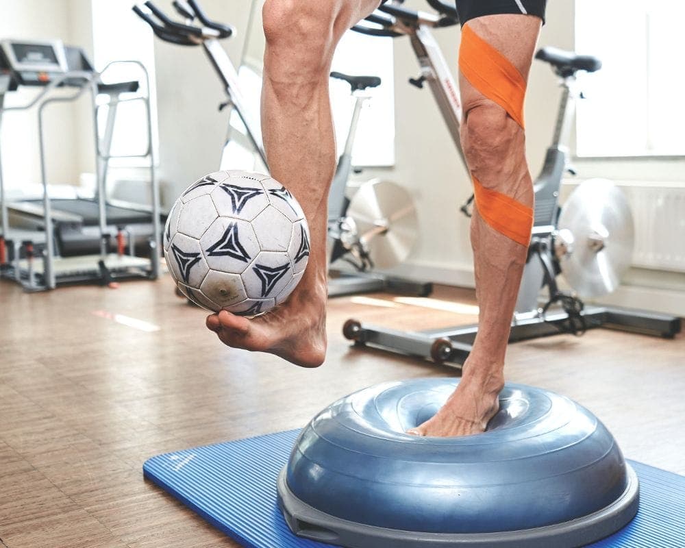 Person balanciert auf einer Balance-Kissen-Kuppel, während ein Ball auf dem angehobenen Fuß liegt